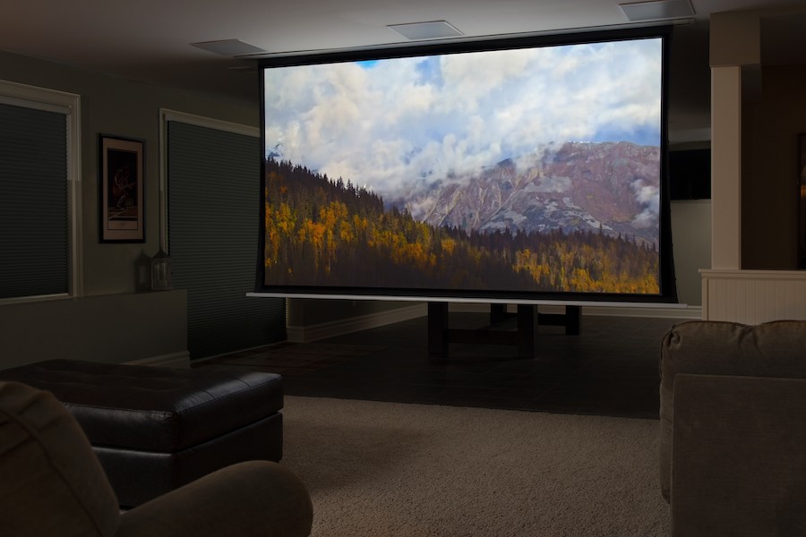 Home theater with cushioned seating and a motorized projection screen in the lowered position