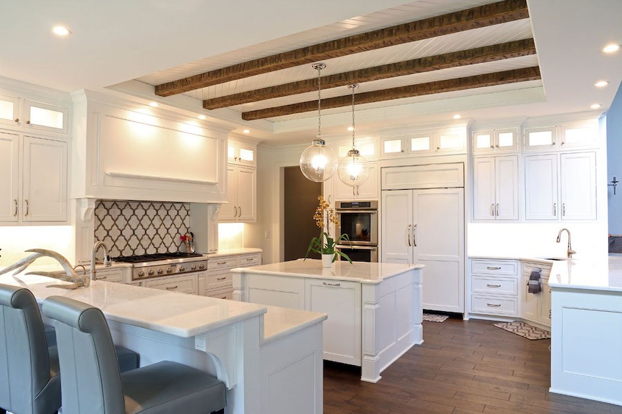 large white kitchen with pendant lighting above the island and hanging from wooden beams in the ceiling.