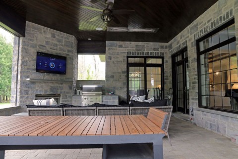 outdoor entertainment area under a covered porch. A grill, TV, and seating are in the background.